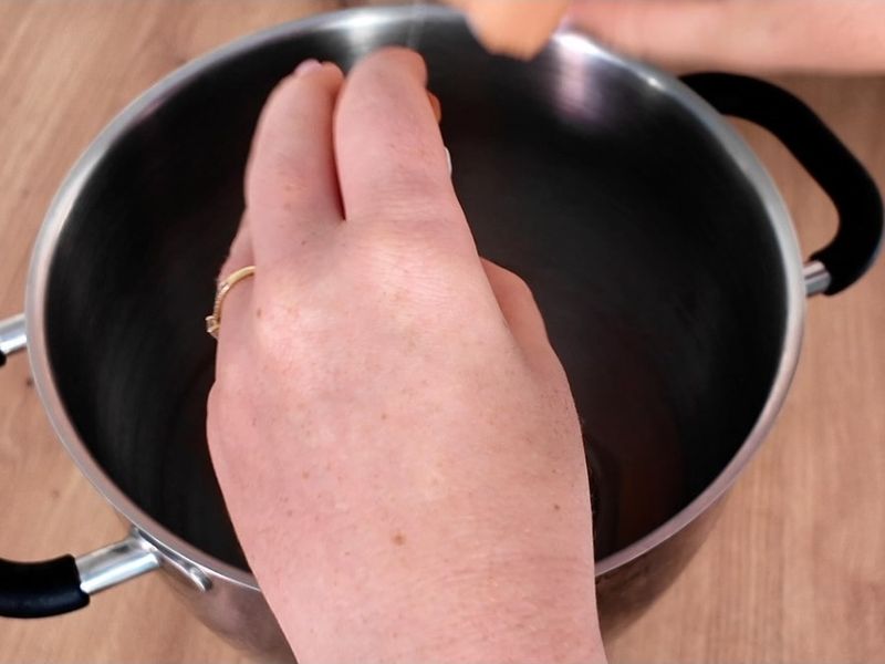 Les mains de la pâtissière au-dessus d'une casserole, dans sa cuisine