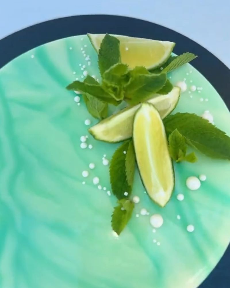Un entremets mojito vu du dessus, glaçage miroir vert menthe, quartiers de citron vert, feuilles de menthe et perles blanches