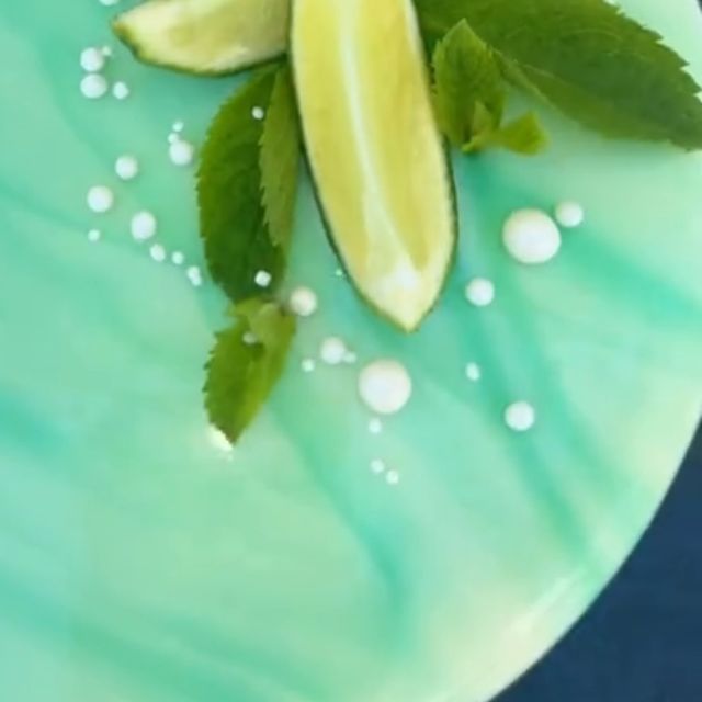 Le glaçage miroir vert menthe d'un entremets mojito, un quartier de citron vert, de la menthe et des perles blanches